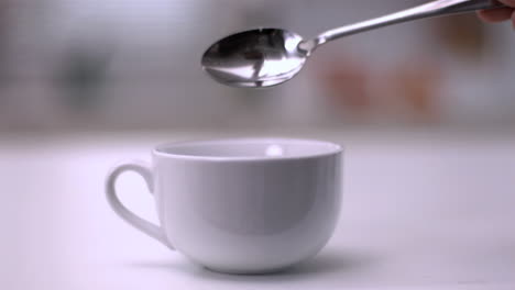 Sugar-cube-falling-from-teaspoon-into-a-white-cup-