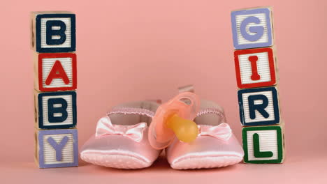 Pink-soother-falling-onto-baby-shoes-besides-baby-blocks