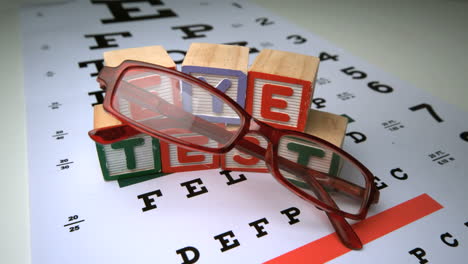 Glasses-falling-onto-eye-test-with-wooden-blocks-spelling-out-eye-test