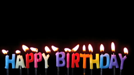 Colourful-happy-birthday-candles-being-blown-out-on-black-background