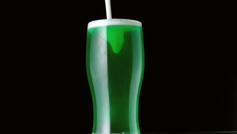 Foam-pouring-onto-pint-of-green-beer-on-black-background