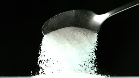Spoon-pouring-white-sugar-on-black-background