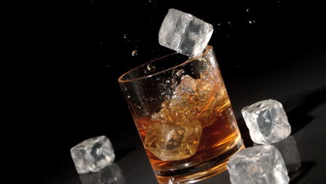 Three-ice-cubes-falling-into-tumbler-of-whiskey-and-ice-