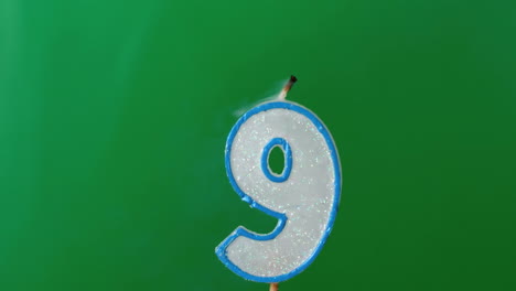 Nine-birthday-candle-flickering-and-extinguishing-on-green-background