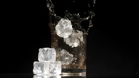 Cubitos-De-Hielo-Cayendo-En-Un-Vaso-De-Whisky-Y-Hielo-Sobre-Fondo-Negro