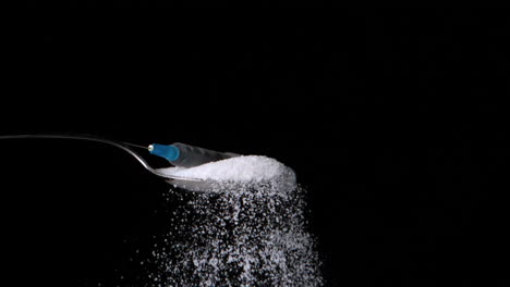 Syringe-falling-onto-spoon-full-of-sugar-on-black-background