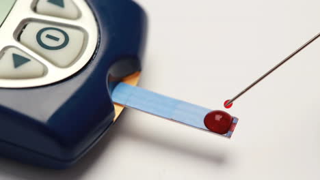 Blutstropfen-Mit-Einer-Spritze-Auf-Den-Teststreifen-Eines-Blutzuckermessgeräts-Aufgetragen