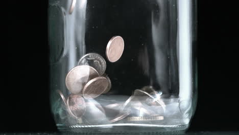 Many-coins-pouring-into-glass-jar-close-up