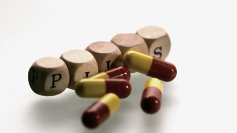Medicine-capsules-falling-in-front-of-dice-spelling-pills
