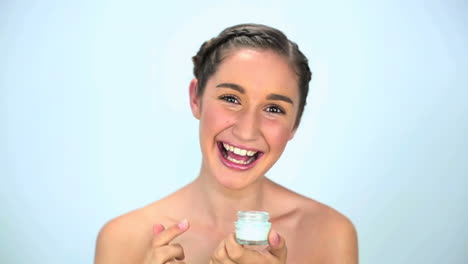 Smiling-young-woman-applying-cream-on-her-face-