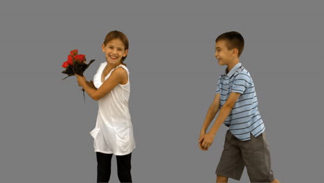 Junge-Bietet-Einem-Kleinen-Mädchen-Auf-Grauem-Bildschirm-Einen-Blumenstrauß-An
