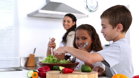 Siblings-making-salad-together-with-mother-watching