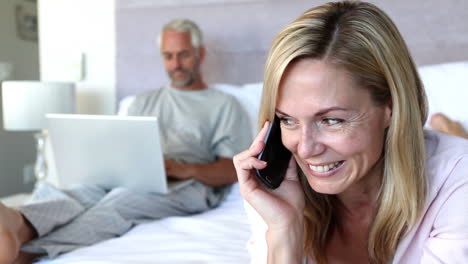 Mujer-Riéndose-Mientras-Habla-Por-Teléfono-Junto-A-Su-Marido-En-Su-Computadora-Portátil