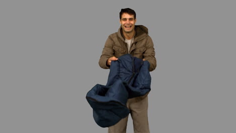 Cheerful-man-rolling-out-his-sleeping-bag-on-grey-screen