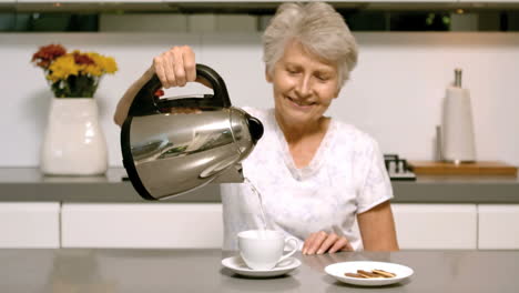 Mujer-Jubilada-Vertiendo-Agua-Hirviendo-De-La-Tetera-En-La-Taza-De-La-Cocina