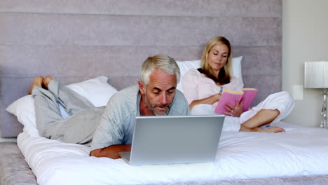 Man-lying-on-his-bed-with-a-laptop-next-to-his-wife