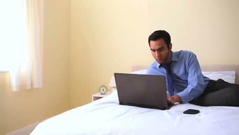 Cheerful-businessman-typing-on-his-notebook-in-bed