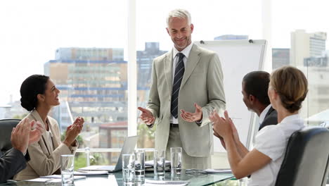 Businessman-presenting-to-his-team-who-applaud-him