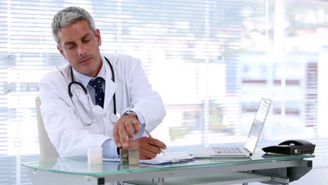 Doctor-looking-at-pills-while-writing-a-prescription