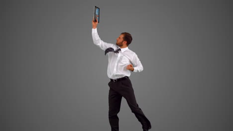 Businessman-holding-tablet-pc-and-jumping-on-grey-background