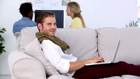 Man-working-on-laptop-on-the-couch-and-smiling