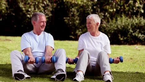 Mature-couple-sat-on-the-grass-lifting-dumbbells