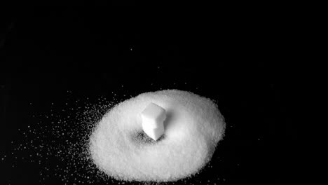 Two-sugar-cubes-falling-into-pile-of-sugar-on-black-surface