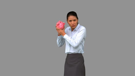 Businesswoman-shaking-an-empty-piggy-bank-on-grey-screen