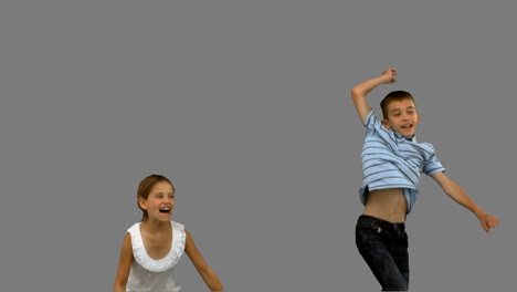 Brother-and-sister-jumping-together-on-grey-screen