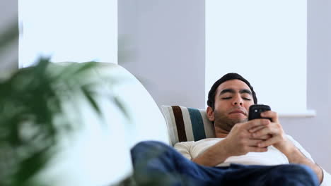 Man-using-his-smartphone-laid-on-a-couch