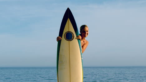 Surfista-Femenina-Asomándose-Desde-Detrás-De-Su-Tabla
