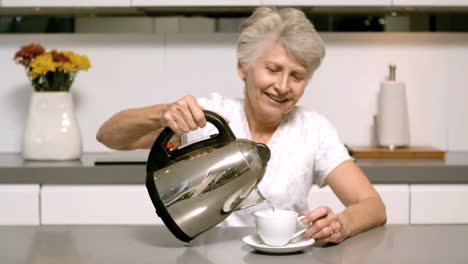Elderly-woman-pouring-boiling-water-from-kettle-into-cup