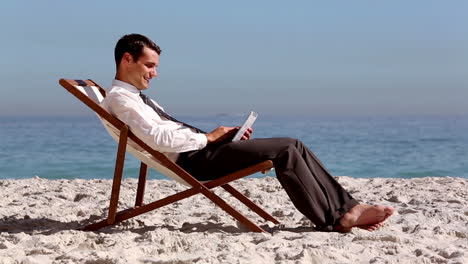 Smiling-businessman-using-tablet-and-relaxing-on-the-beach