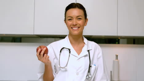 Enfermera-A-Domicilio-Sosteniendo-Manzana-Y-Sonriendo-En-La-Cocina