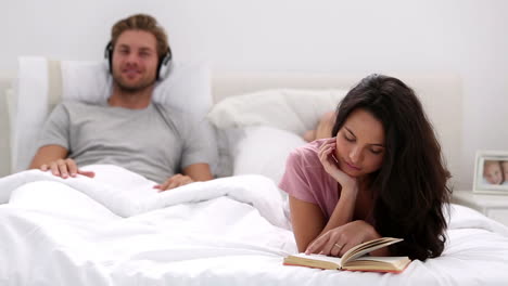 Woman-reading-book-while-partner-is-listening-to-music