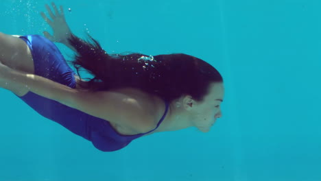 Brünette-Frau-Schwimmt-Unter-Wasser-Im-Blauen-Badeanzug