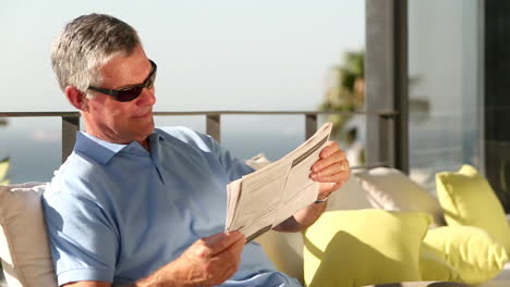 Mature-man-taking-off-his-sunglasses-while-reading-newspaper