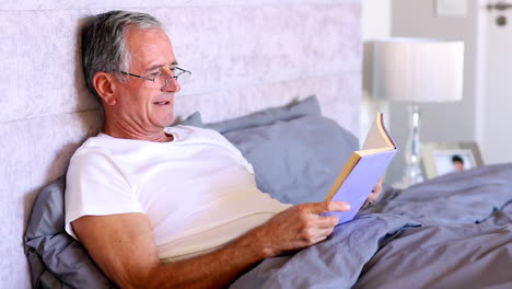 Elderly-man-reading-book-in-bed