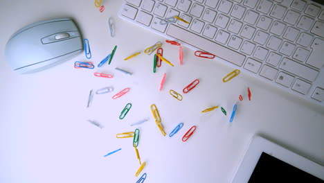 Colourful-paperclips-falling-in-the-middle-of-a-white-office-desk