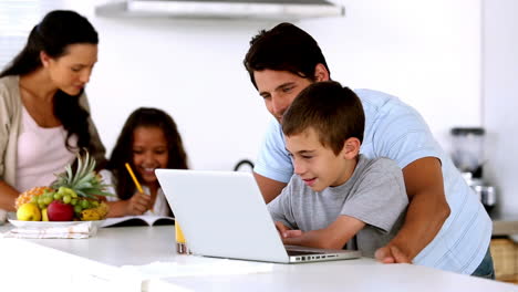 Father-looking-at-laptop-with-son-and-mother-enters-to-help-daughter