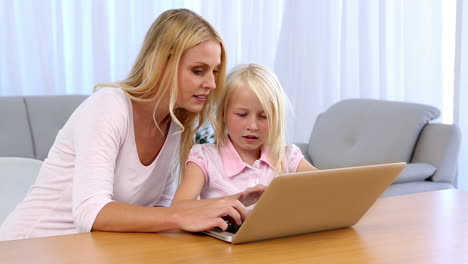 Mother-and-daughter-sitting-at-table-and-using-laptop