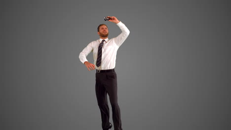 Businessman-leaping-and-taking-self-portrait-on-grey-background