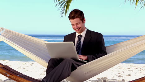 Businessman-typing-on-his-laptop-in-a-hammock-and-smiling