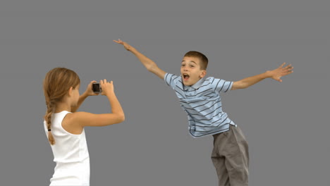 Sister-taking-pictures-of-her-brother-jumping-on-grey-screen