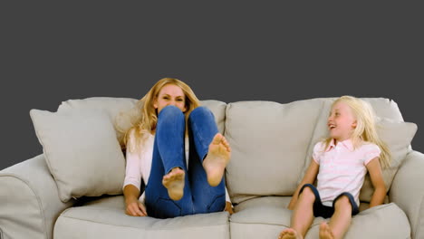 Mother-and-daughter-jumping-on-the-sofa-on-grey-background