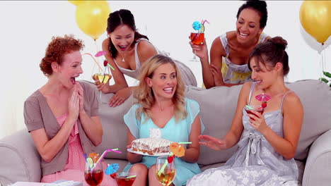 Woman-blowing-out-the-birthday-candles-surrounded-by-her-friends