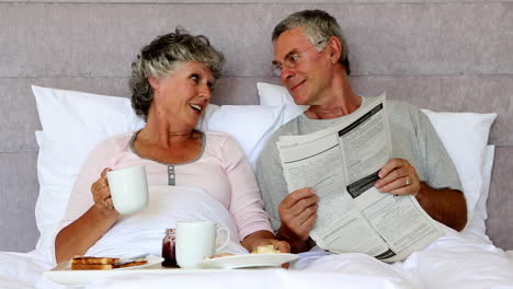 Husband-reading-the-newspaper-to-his-wife-during-breakfast-