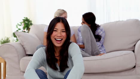 Smiling-woman-sat-on-the-floor-with-friends-chatting-behind