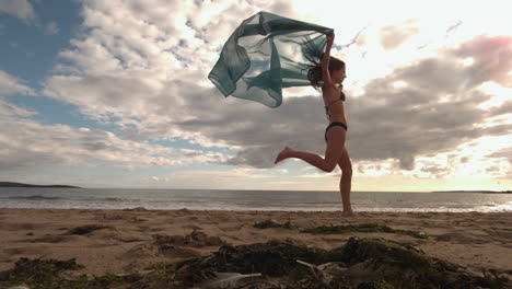 Mujer-Saltando-En-La-Playa-Sosteniendo-Una-Bufanda