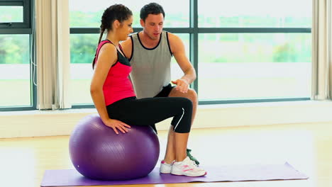Pretty-woman-training-sitting-on-fitness-ball-with-coach